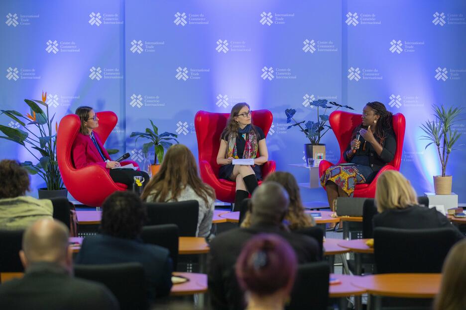 Three people in red chairs speak on stage at a conference